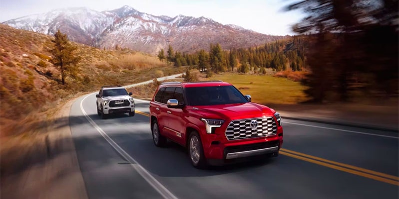 Two 2024 Toyota Sequoia SUVs driving down a beautiful country road in Akron, OH