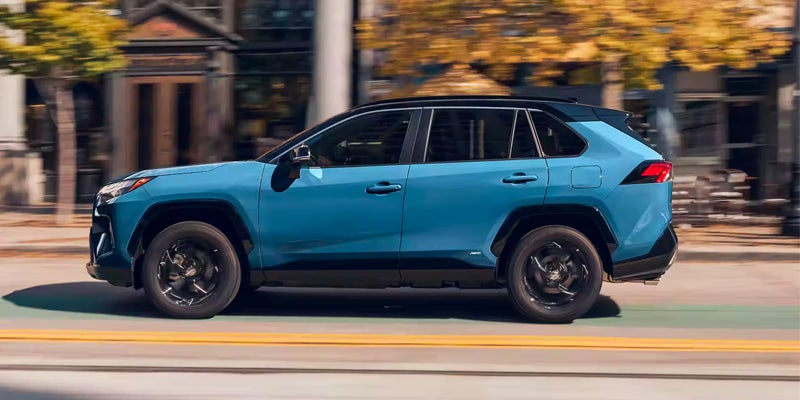 A side view of the 2024 Toyota RAV4 Hybrid driving down a blurry street in Akron, OH